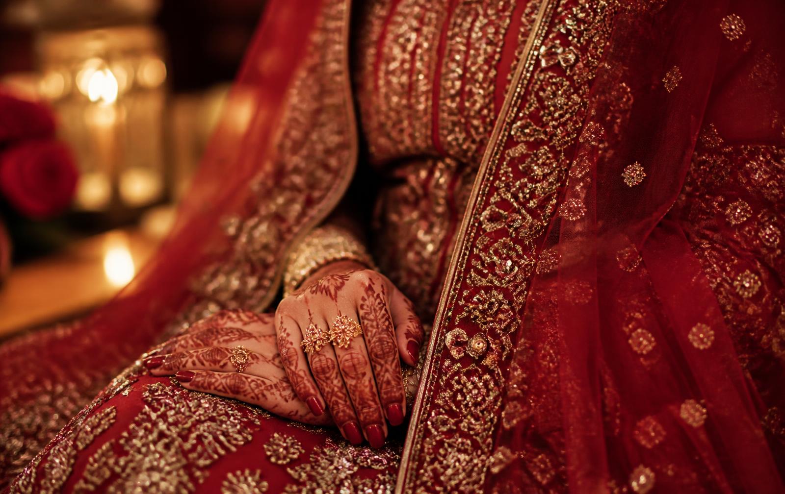 Bride's henna hands with a gold ring on a crimson bridal dress